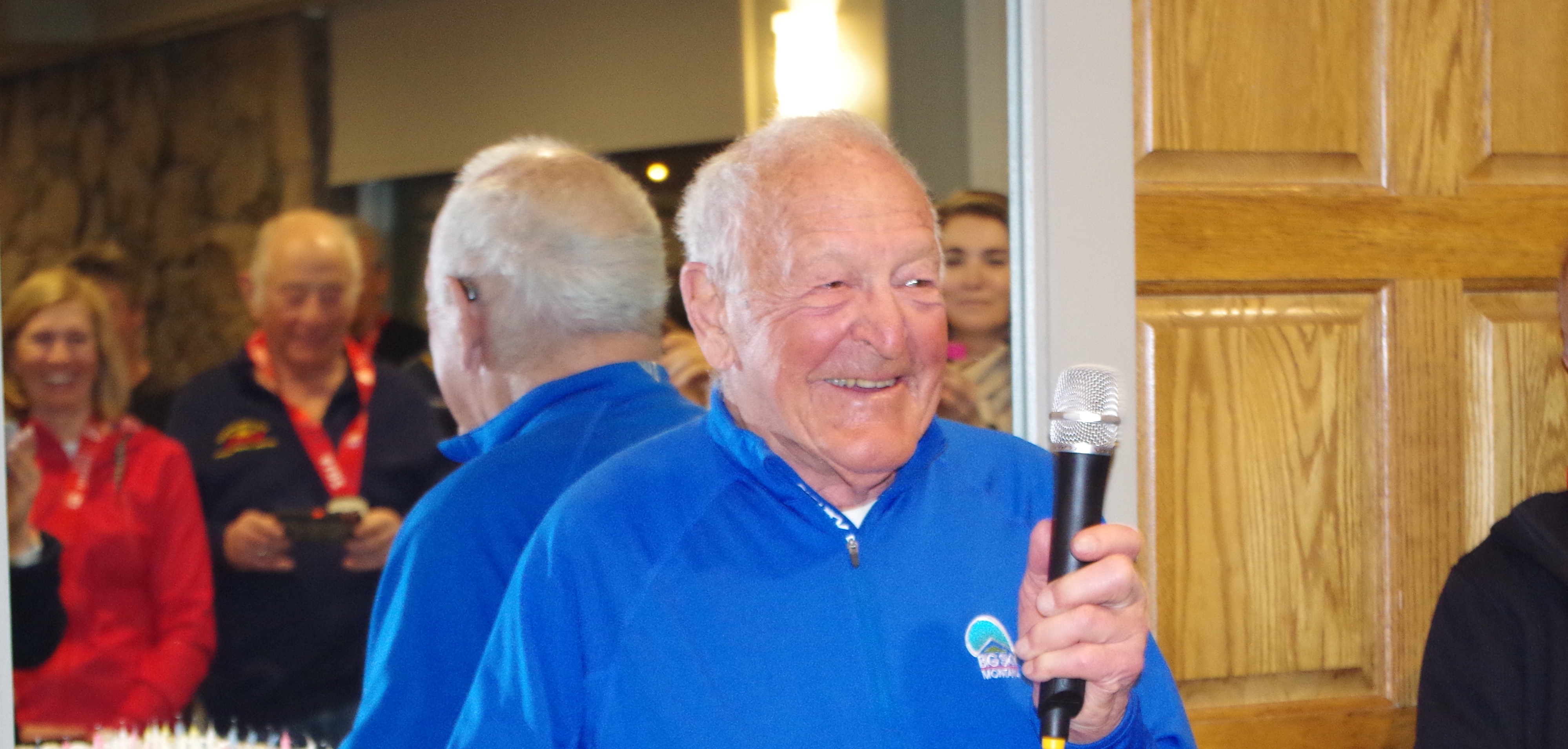 Gate holding a microphone and addressing the crowd at his 90th birthday celebration at the 2019 FIS Masters Cup in Aspen