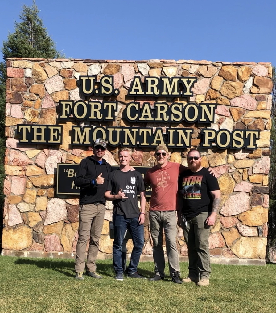 Jason Wolle with Jesse Stewart and friends at Fort Carson. (U.S. Ski and Snowboard) Jason Wolle in front of Fort Carson sign.