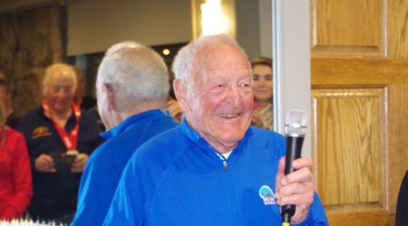 Gate holding a microphone and addressing the crowd at his 90th birthday celebration at the 2019 FIS Masters Cup in Aspen
