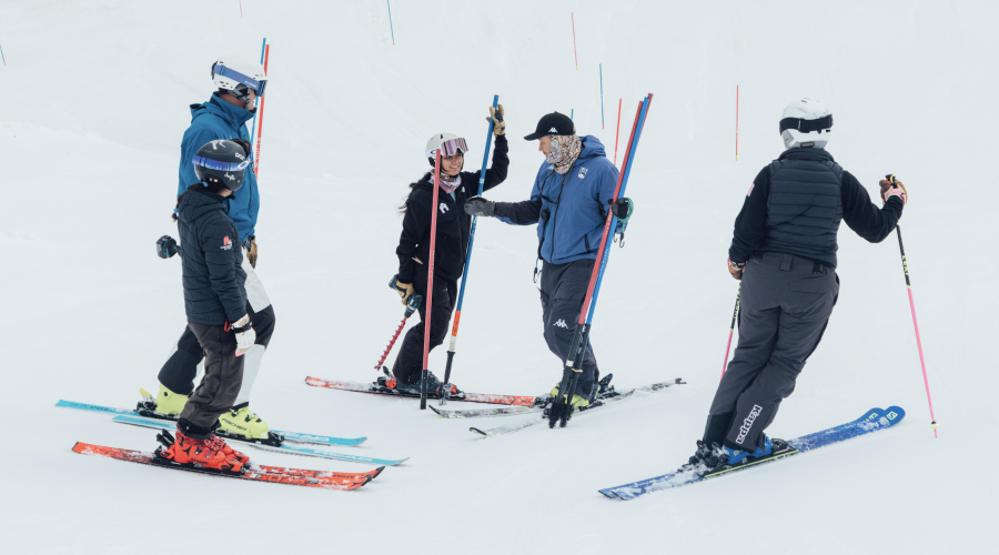 Five alpine coaches stand together on the snow in the process of setting a slalom course